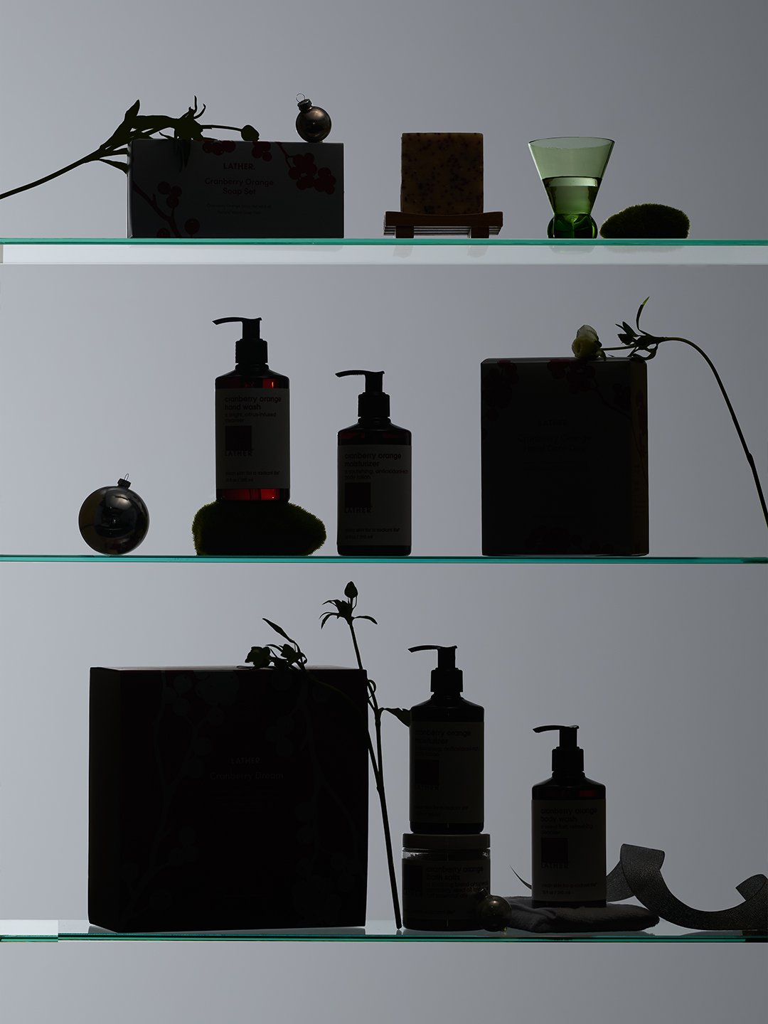 A darkly underexposed teaser shot of the Cranberry Orange shelf display — the soap set, hand wash and lotion duo, hand care duo box, and Cranberry Dream box rendered as near-silhouettes.