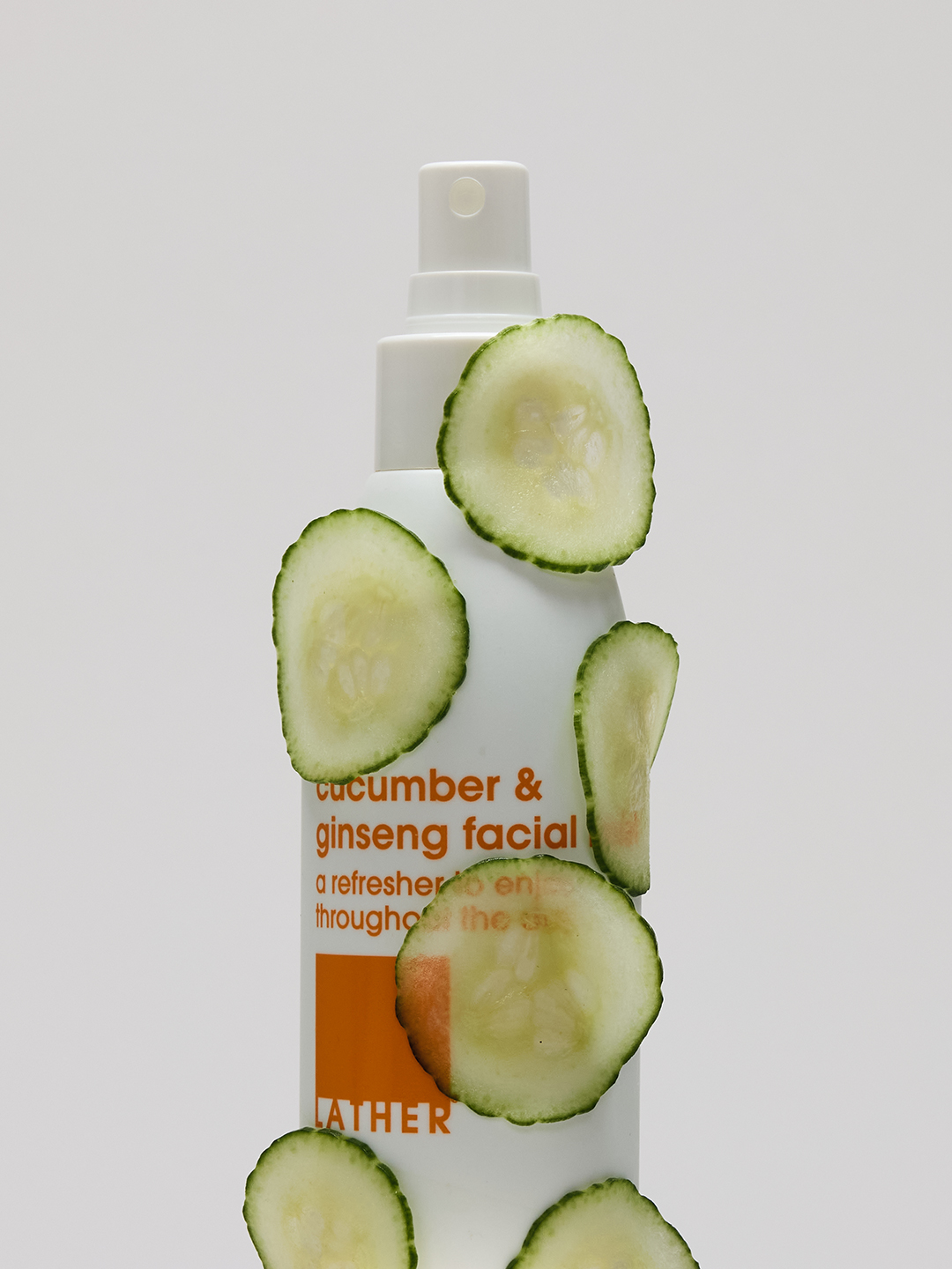 A bottle of Lather cucumber & ginseng facial mist scattered with fresh cucumber slices.