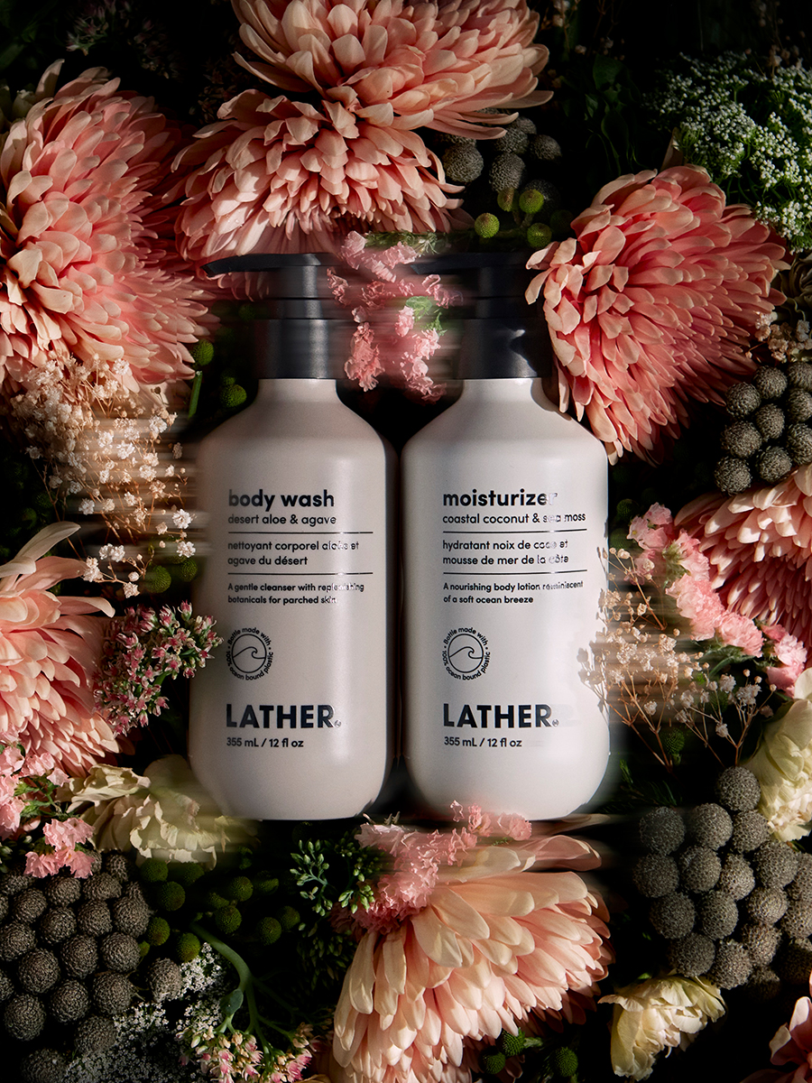 Lather body wash and moisturizer bottles nestled amid pink and cream dried flowers and thistle.