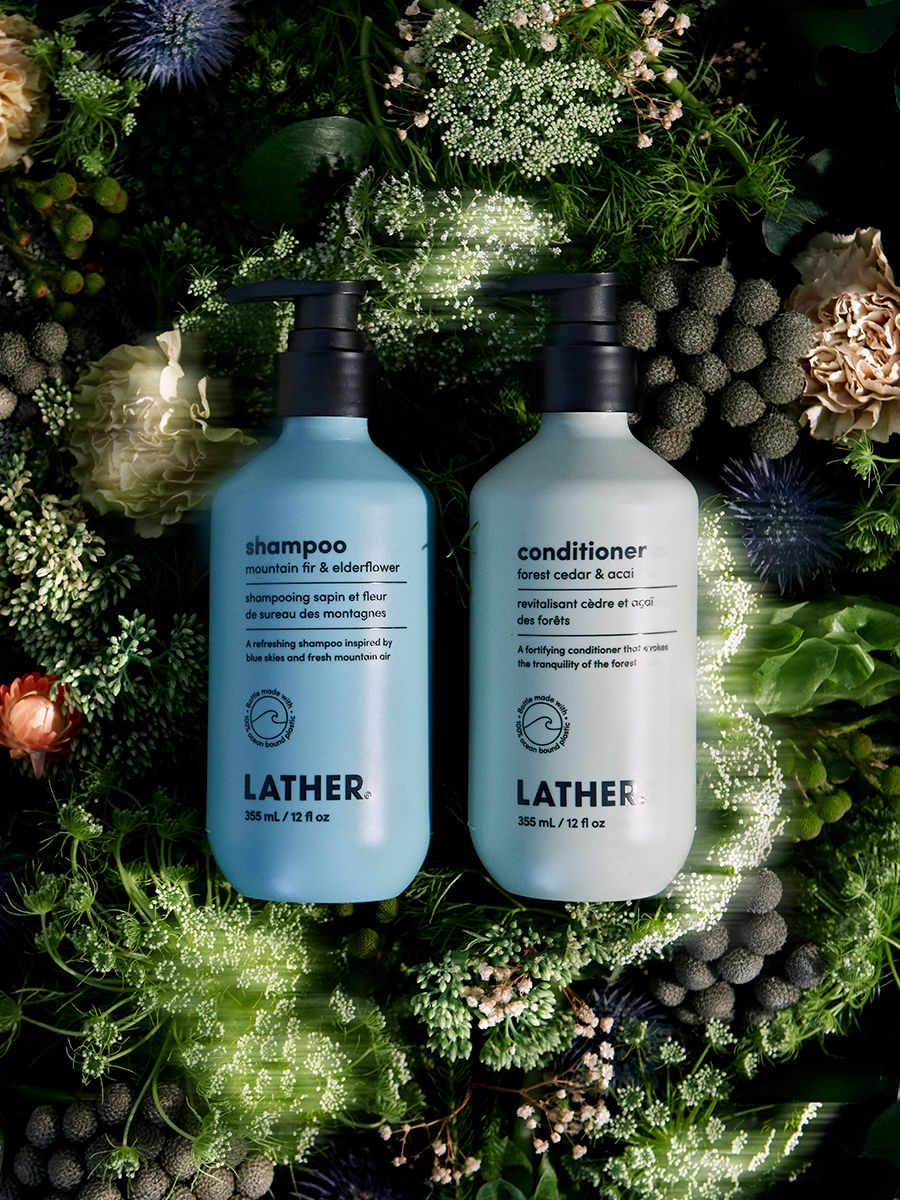 Lather shampoo and conditioner bottles nestled in blue thistle and white florals with dark greenery.