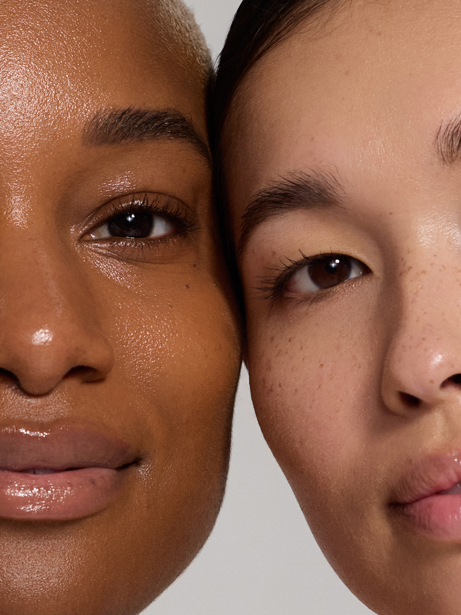 Two models face to face in extreme close-up, eyes and lips nearly touching, showing contrasting skin tones and freckles.