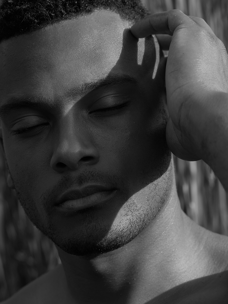 Black-and-white profile portrait of a man with eyes closed, sunlight and shadow cutting across his face.
