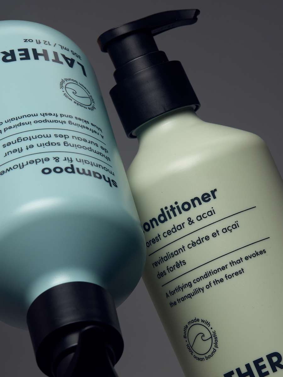 Close-up of Lather shampoo and conditioner bottles in teal and sage, angled together against a grey background.