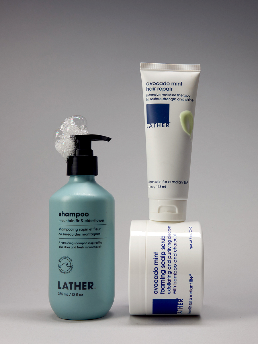 A teal bottle of Lather mountain fir & elderflower shampoo beside a tube of avocado mint hair repair and a tub of avocado mint foaming scalp scrub.