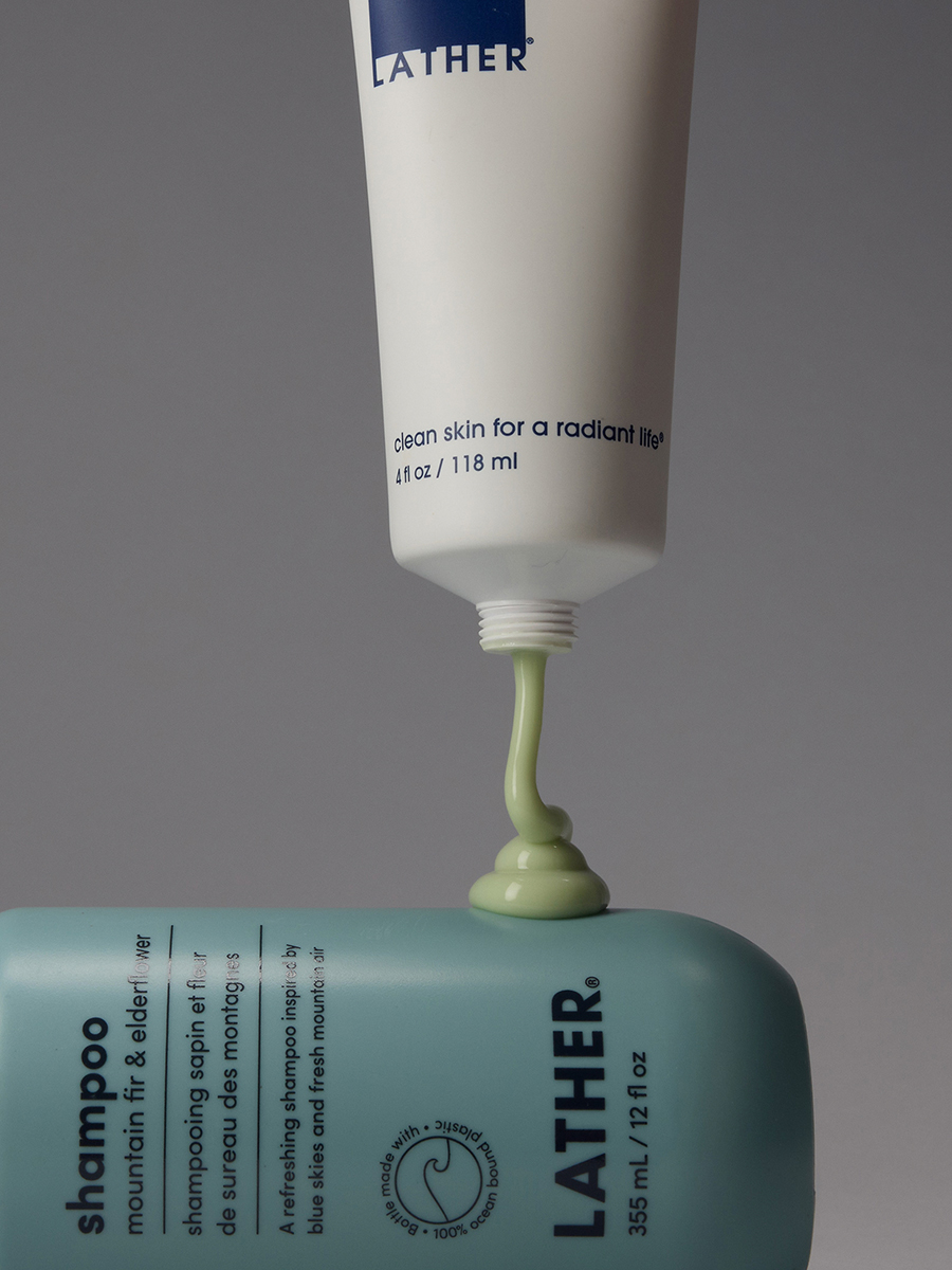 A tube of Lather mountain fir & elderflower shampoo poured onto its avocado mint hair repair tube, pale green product dripping down.