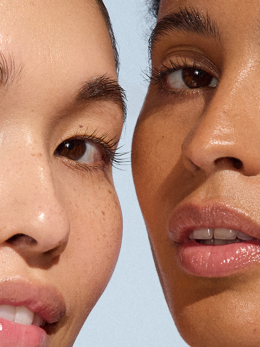 Two models' faces side by side in extreme close-up — one showing a freckled eye and brow, the other a nose and glossy open lips.