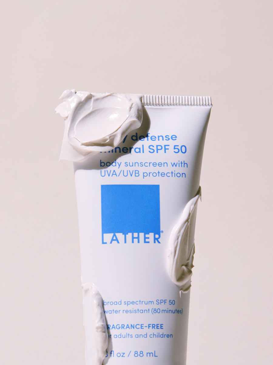 Close-up of a tube of Lather daily defense mineral SPF 50 with sunscreen cream smeared across its cap and sides.