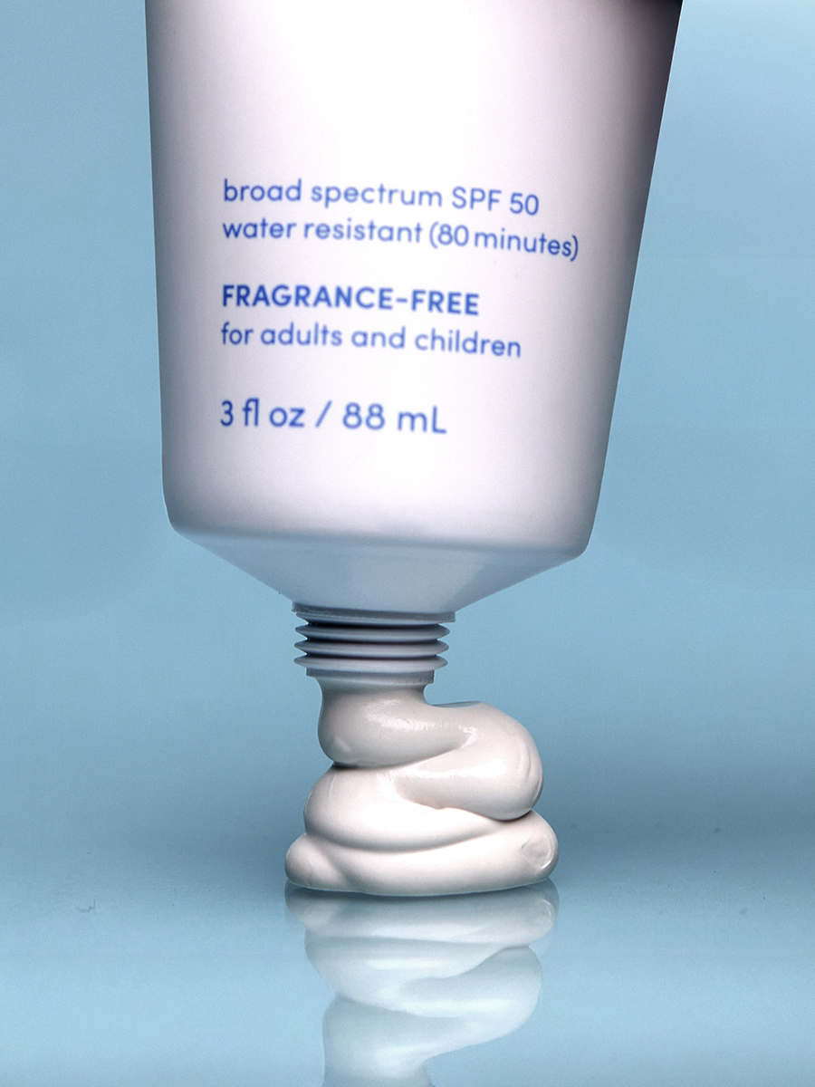 Close-up of a tube of Lather daily defense mineral SPF 50 with a swirl of sunscreen cream at its base, set against a pale blue background.