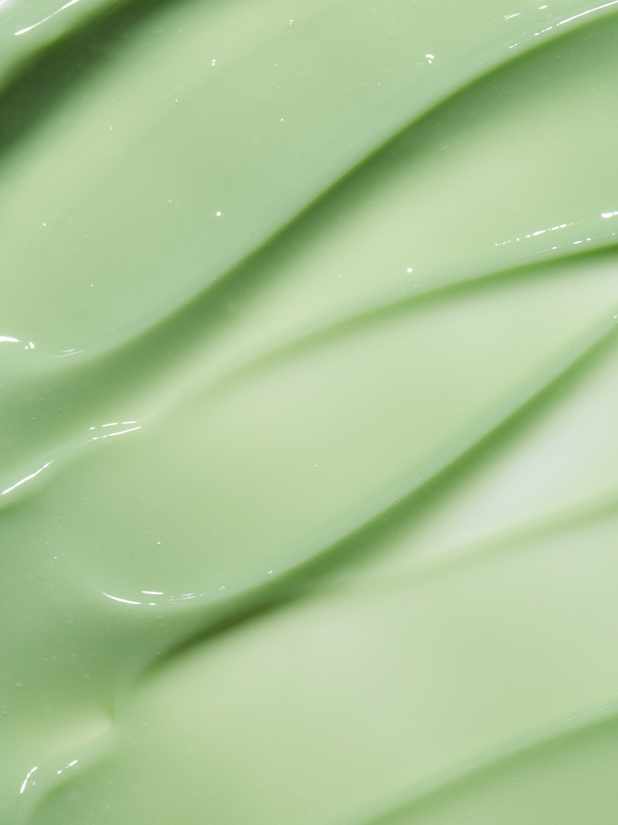 Macro close-up of a swirled pale green cream texture, its ridges catching soft light.