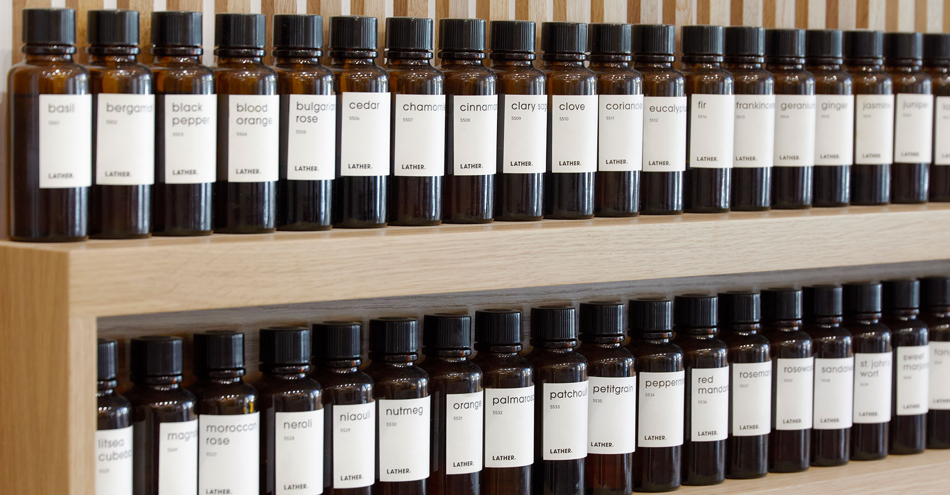 Rows of amber glass essential-oil bottles with cream labels mounted on an oak slat wall, forming the store's apothecary-style fragrance bar.
