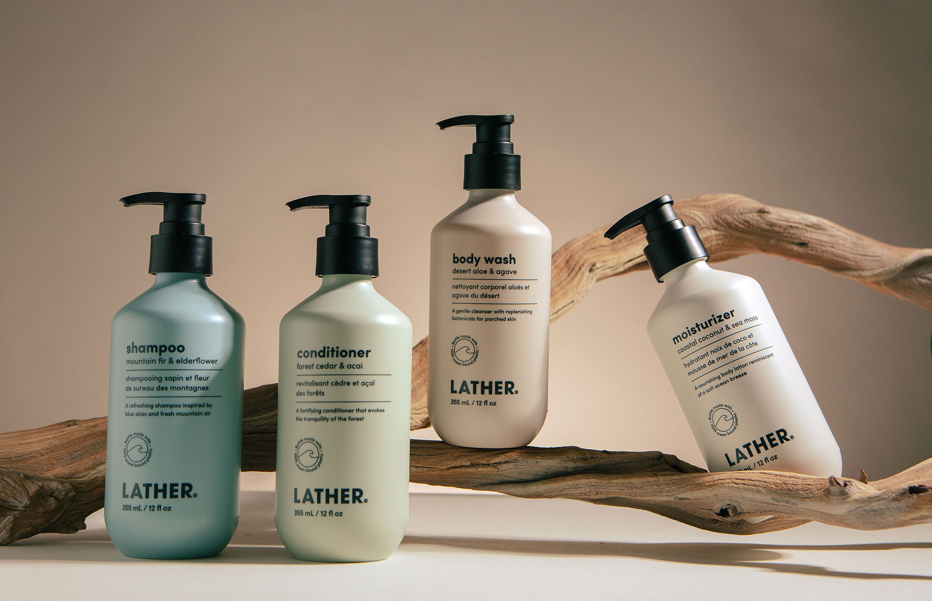 The Landscapes Collection bottles — shampoo, conditioner, body wash, and moisturizer — arranged along a piece of weathered driftwood against a warm neutral backdrop.