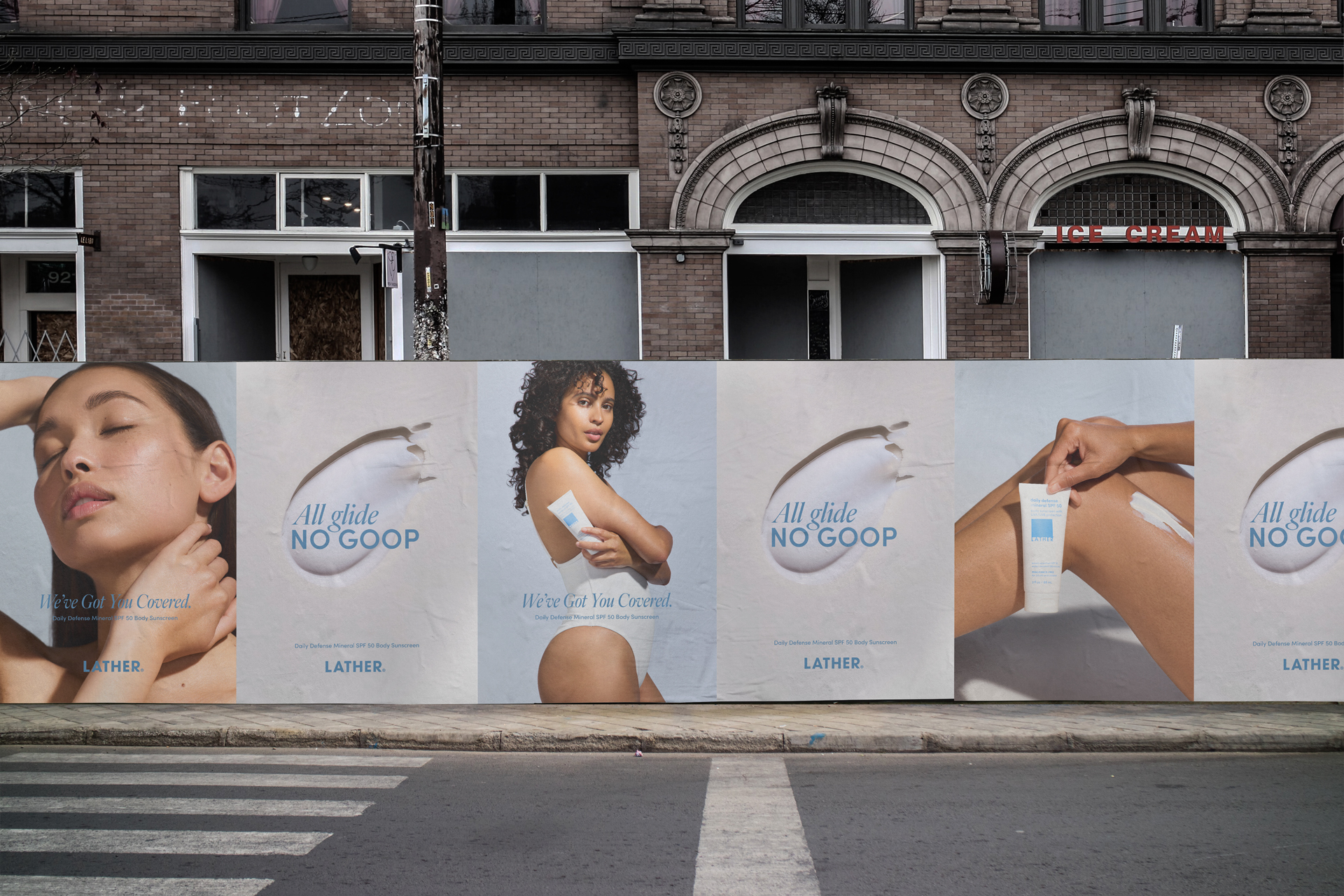 Photograph of LATHER Daily Defense SPF 50 wheatpasted street posters lining a storefront wall, alternating a model's portrait with the 'All Glide, No Goop' cream graphic and product application shots.