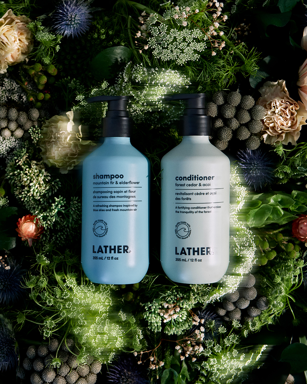 Lather shampoo and conditioner bottles nestled in a bed of greenery and dried florals.