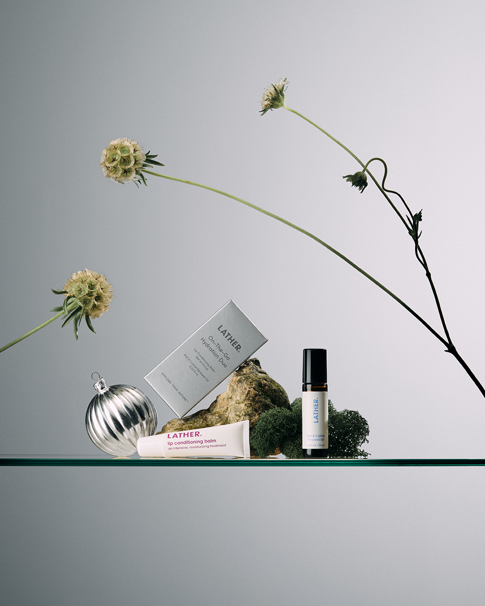 Lather holiday gift set styled with dried florals, a silver ornament, and a sprig of greenery on a glass shelf.