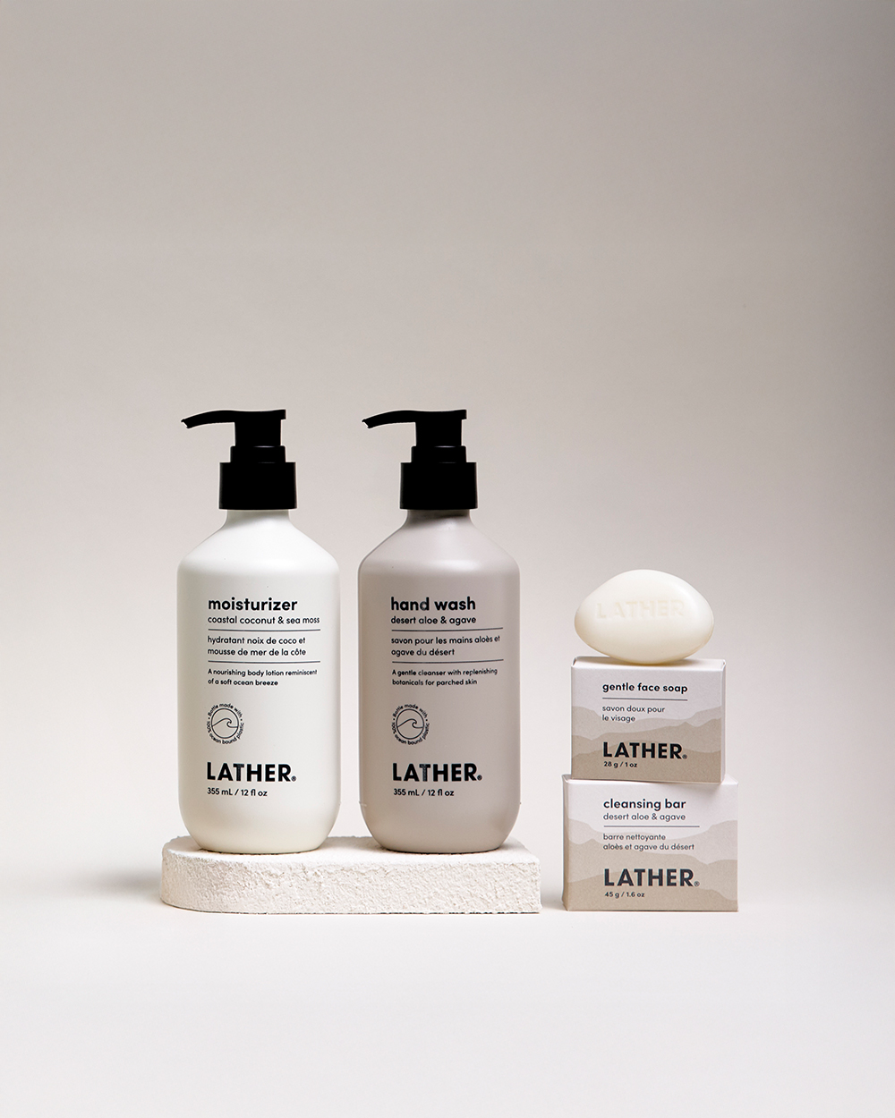 Lather hotel amenity moisturizer and hand wash bottles beside a stacked soap bar and boxed face soap.